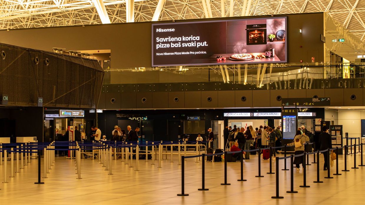 SEO versus PPC: travelers check in at Zagreb Airport with large advertising screen above